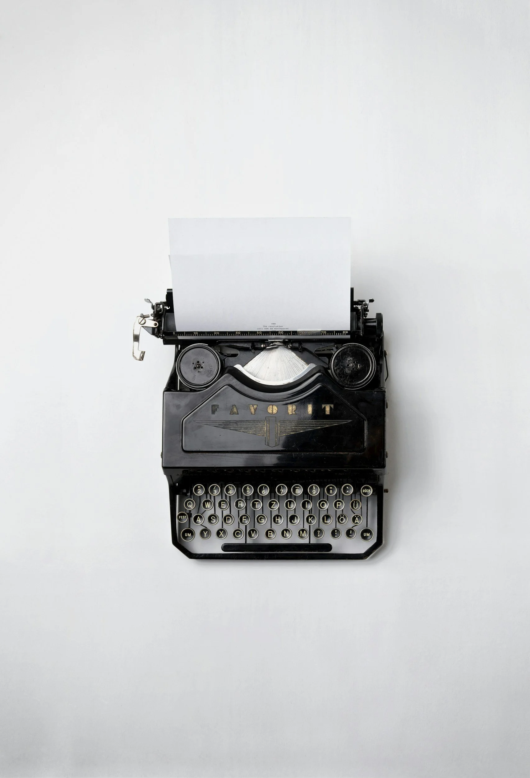 A vintage black typewriter with white keys, set against a plain white background, with a blank sheet of paper inserted.